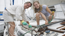 A smiling couple lean into the shot next to their sailboat.